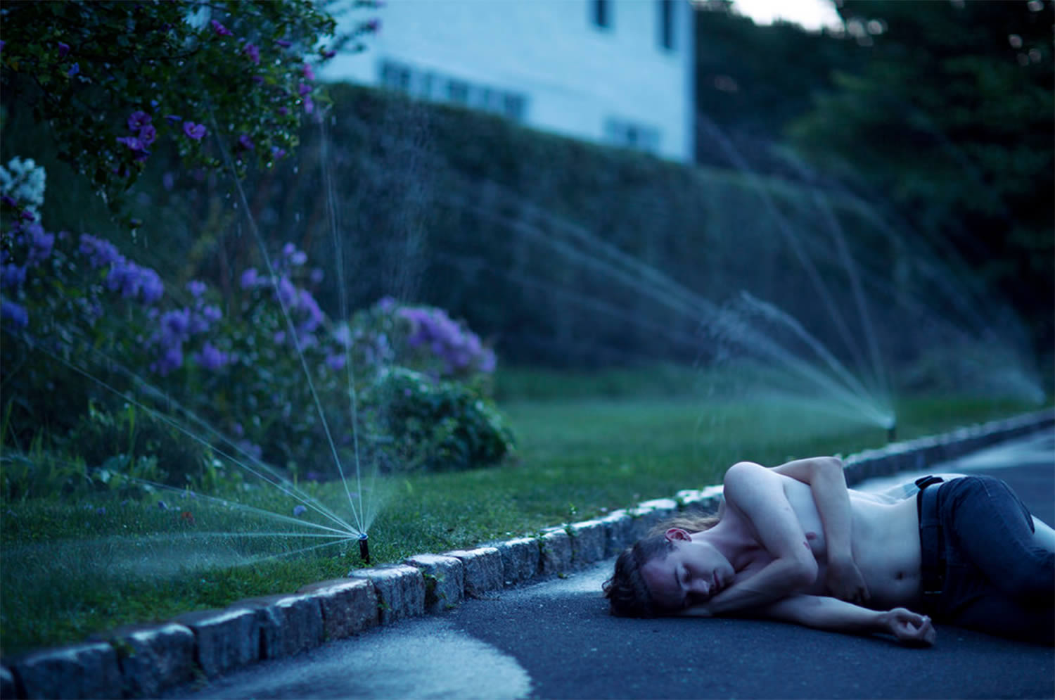 man lying on ground, sprinklers on, "Sunrise Dream" by Olivia Bee.
