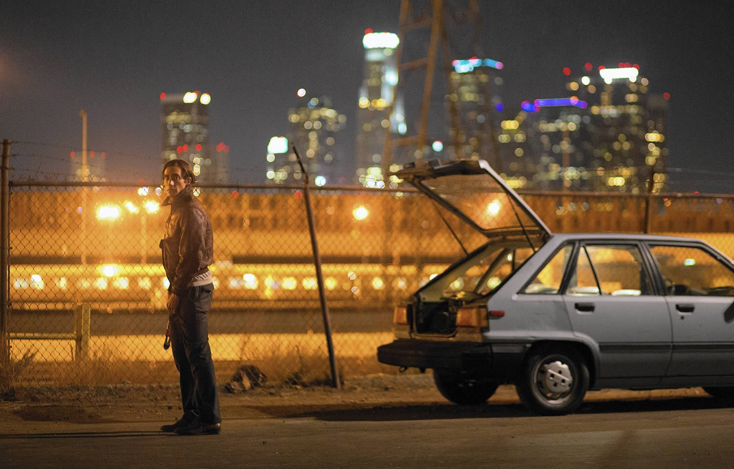 Jake Gyllenhaal beside a car with cityscape in back, nightcrawlers movie