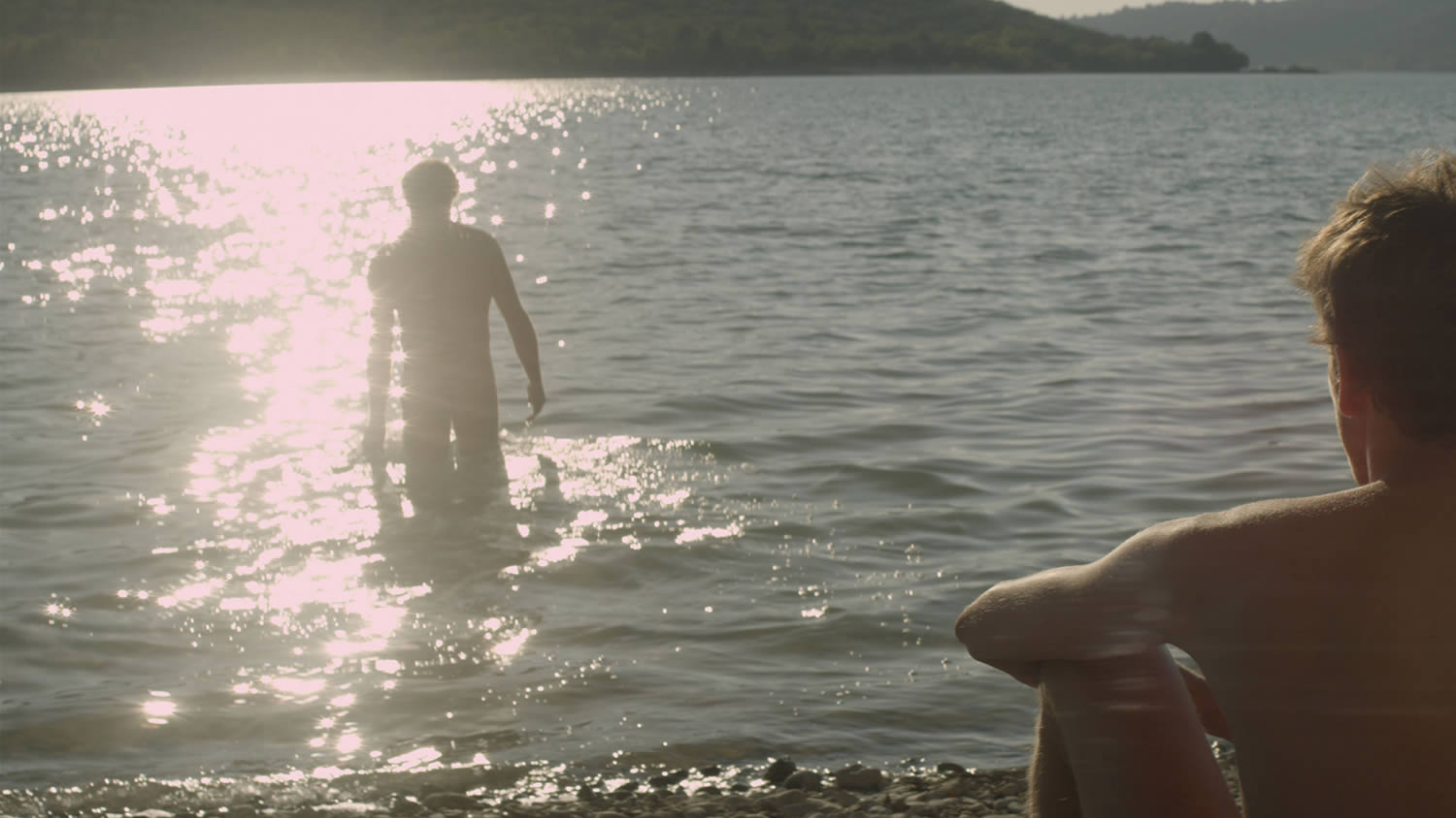 man watching another man walk into a lake