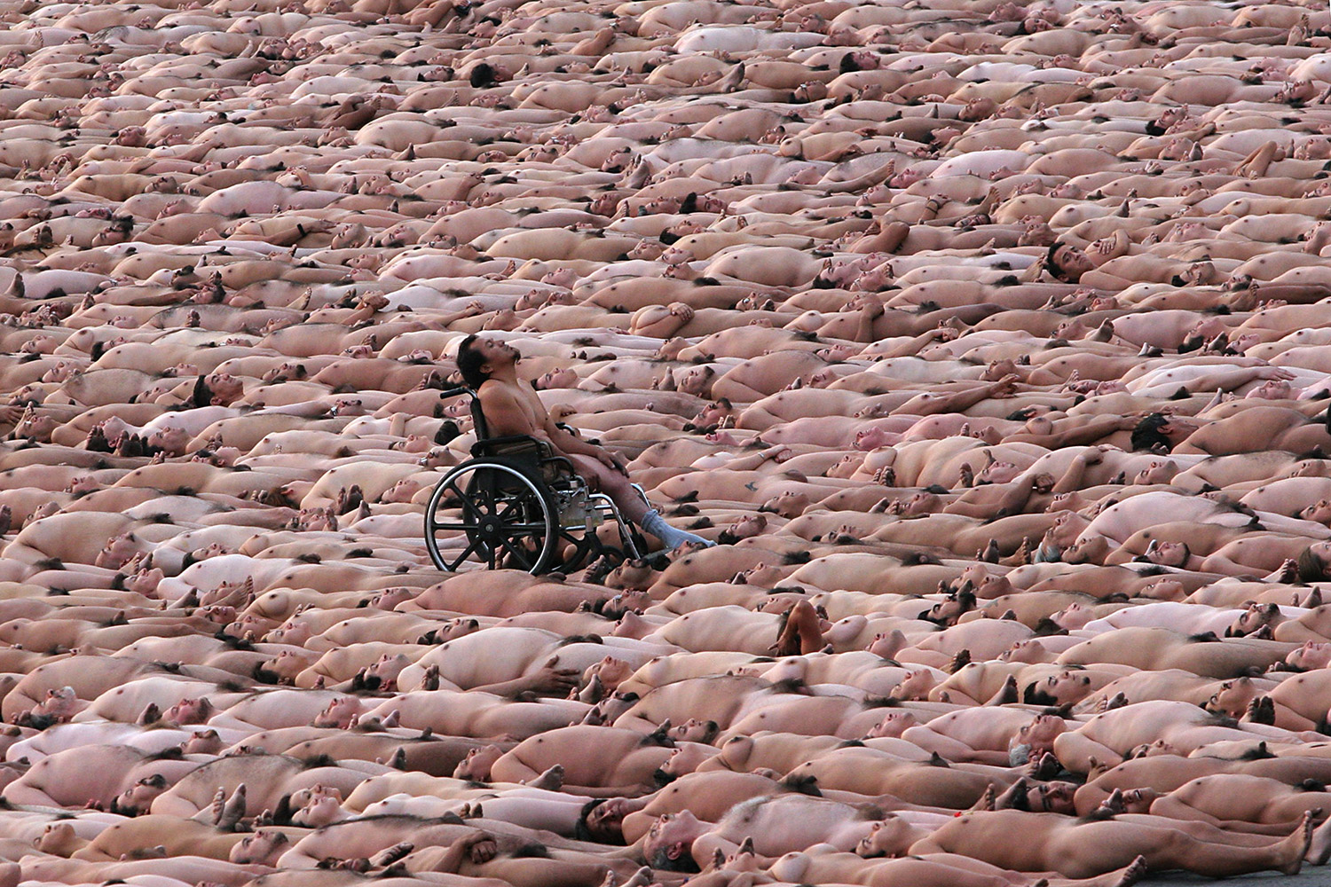 Spencer Tunick - photographs of nude bodies lying down, surrounding man in wheelchair
