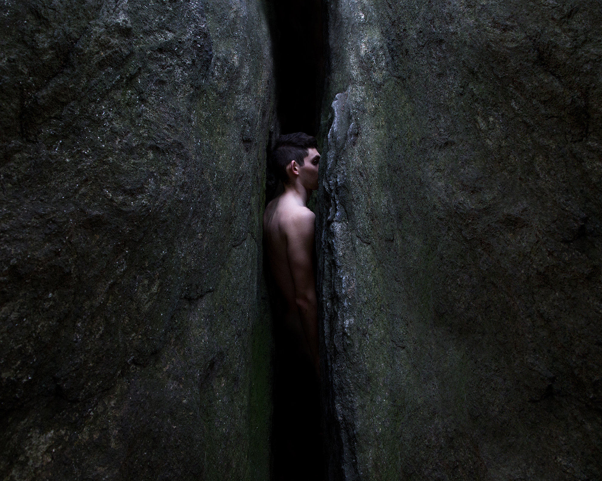 male nude stuck between large rocks, by ben zank