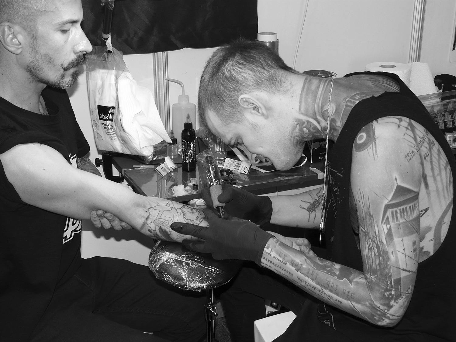 Neon Judas tattooing client's arm