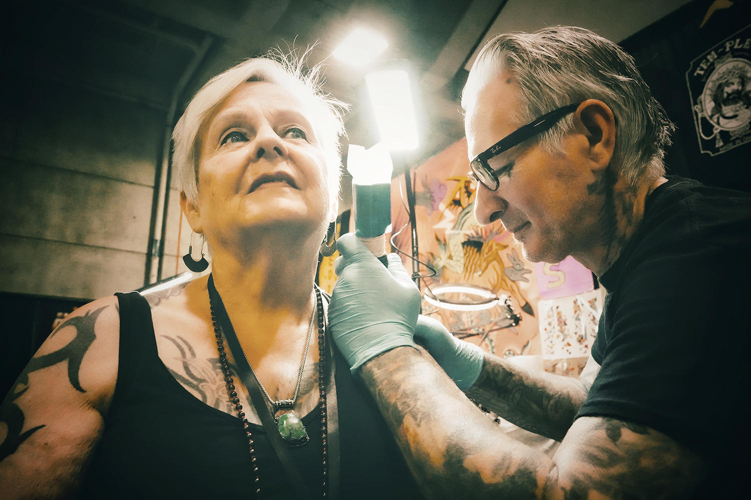 Freddy Corbin tattooing a delicate rose on the shoulder of master photographer Diane Mansfield