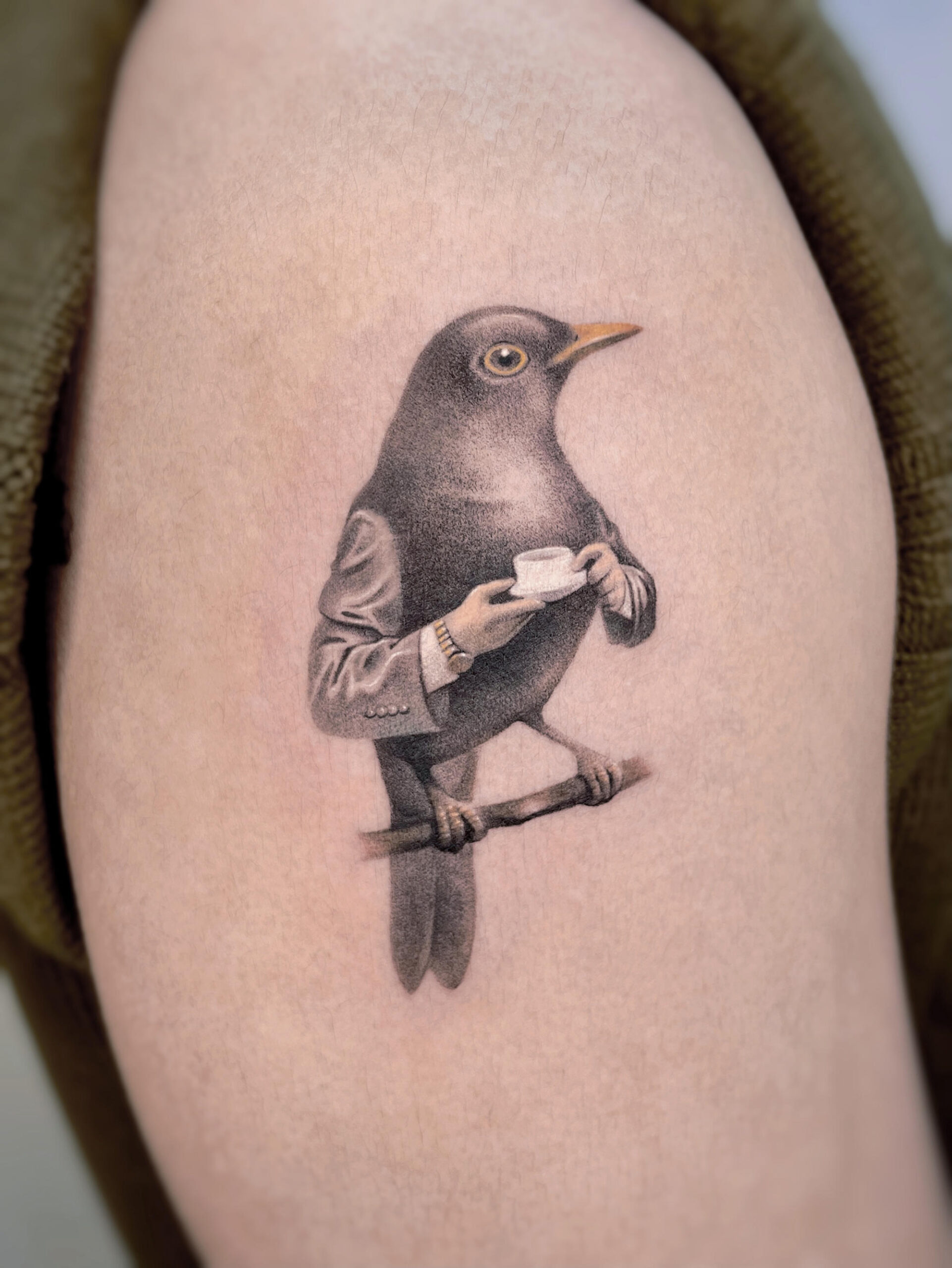 A tattoo by Gyan of a Victorian bird character sipping tea