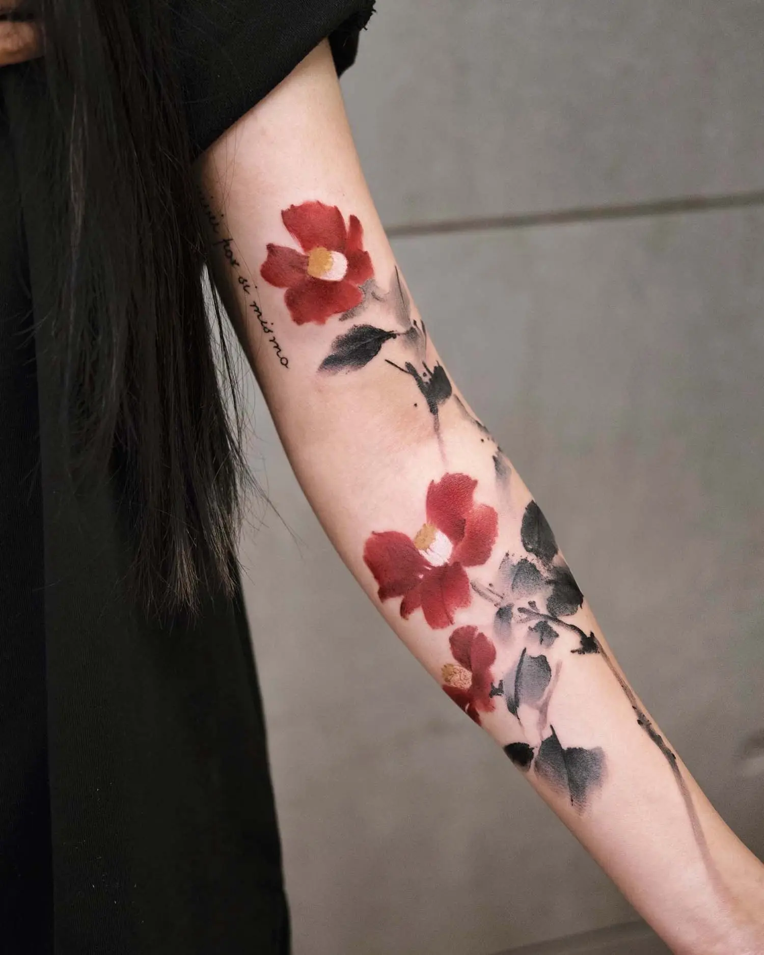 This tattoo features vibrant red passion camellias with delicate, painterly textures