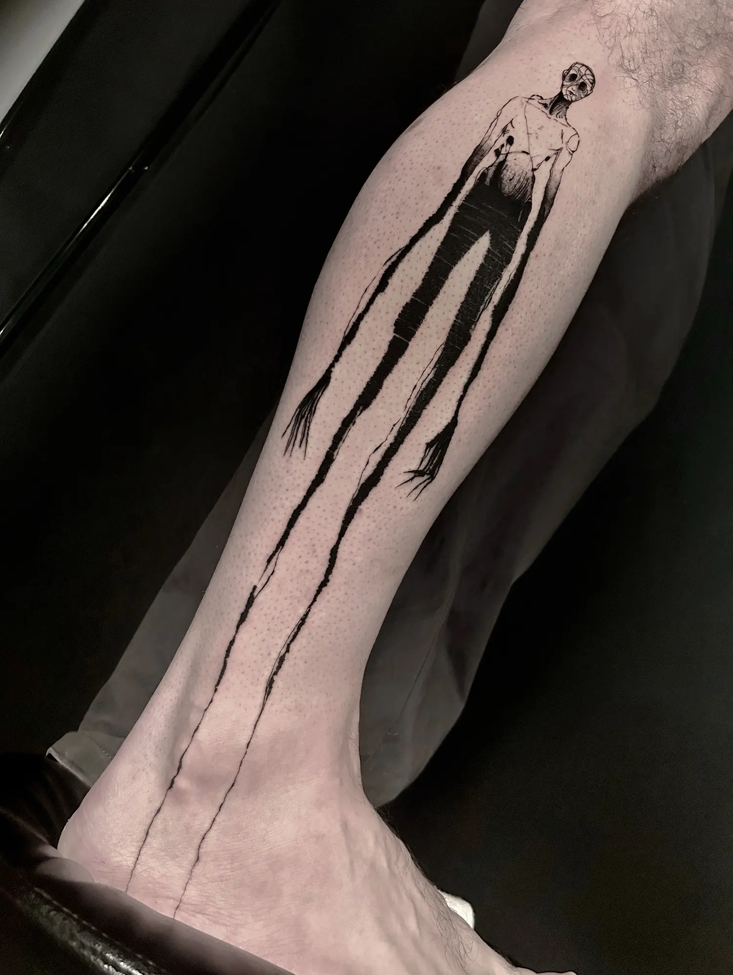 a tattoo of a stretched person, called hollow, black ink tattoo on leg